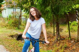 ung kvinna ridning cykel i sommar stad parkera utomhus. aktiva människor. hipster flicka koppla av och ryttare cykel. cykling till arbete på sommar dag. cykel och ekologi livsstil begrepp. foto