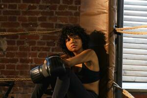 kvinna kämpe flicka kraft. afrikansk amerikan kvinna kämpe med boxning handskar Sammanträde på boxning ringa väntar och vilar efter bekämpa. stark kraftfull flicka i Gym. styrka passa kropp träna Träning. foto
