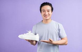 asiatisk man som håller sneakers på lila bakgrund foto