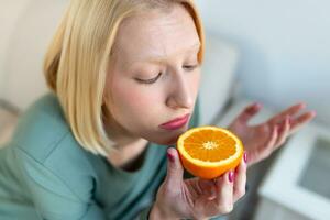 sjuk kvinna påfrestande till känsla lukt av halv färsk orange, har symptom av covid19, korona virus infektion - förlust av lukt och smak. ett av de huvud tecken av de sjukdom. foto