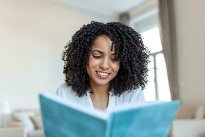 ung skön afrikansk amerikan kvinna innehav bok, universitet studerande studerar, inlärning språk. fritid, litteratur och människor begrepp - leende afrikansk amerikan kvinna läsning bok på Hem foto
