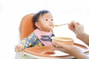 6 månader gammalt behandla som ett barn flickan som äter blandningsmat på en barnstol. foto