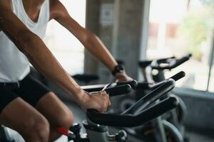 stänga upp händer av asiatisk sportsman utövar på en cykel i de Gym, bestämning till konditionsträning tappa bort vikt, gör henne friska. övning cykel man kondition sport begrepp. foto