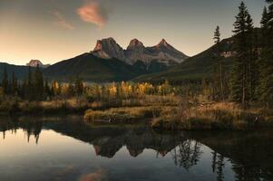 landskap av tre systrar bergen reflexion på höst skog i de morgon- på Canmore, banff nationell parkera foto