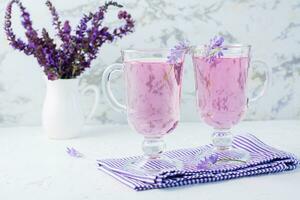 färsk vatten med lavendel- i glasögon och en bukett av blommor i en kanna på de tabell. lavendel- aromatisk cocktail foto