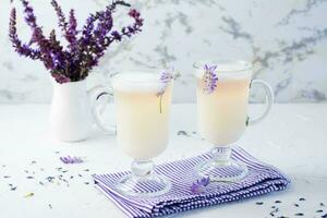 kaffe med mjölk, skum och lavendel- i glasögon och en bukett av blommor i en kanna på en vit tabell foto