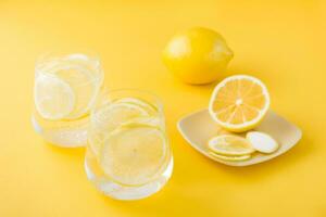 gnistrande vatten med citron- och is i glasögon och citron- skivor på en fat på en gul bakgrund. detox dryck foto