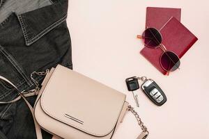 framställning för en bil resa. pass, solglasögon, bil nycklar, väska och denim jacka på en rosa bakgrund. lokal- turism. topp se foto