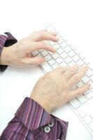 händer av ett gammal kvinna skriver på de tangentbord, isolerat på vit, närbild. foto