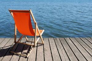 tömma vikbar strand stol på trä- däck utsikt lugna vatten sjö foto