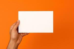 en mänsklig hand innehav en tom ark av vit papper eller kort isolerat på orange bakgrund. ai genererad foto