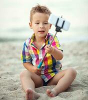 barn med telefon och selfie pinne på de strand foto