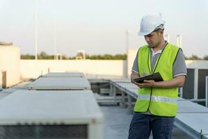 asiatisk underhåll ingenjör Arbetar på de tak av fabrik. entreprenör inspektera kompressor systemet och planer installation av luft tillstånd system i konstruktion. checklista, inspektör, kontrollera foto