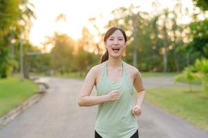 passa asiatisk ung kvinna joggning i parkera leende Lycklig löpning och njuter en friska utomhus- livsstil. kvinna joggare. kondition löpare flicka i offentlig parkera. friska livsstil och wellness varelse begrepp foto