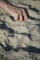 närbild av händer med sand faller på en strand foto