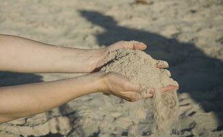 närbild av händer med sand faller på en strand foto