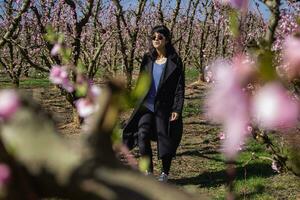 kvinna gående genom fält av blommande persika träd i vår. foto