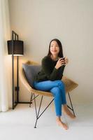 porträtt vacker ung asiatisk kvinna hålla kaffekopp och sitter på soffa stol foto