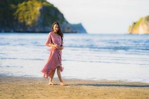 porträtt ung vacker asiatisk kvinna gå leende och glad på stranden havet och havet foto
