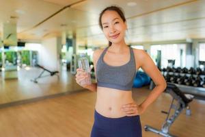 stående vacker ung asiatisk kvinna med flaskvatten i gymmet foto