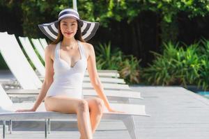 porträtt vacker ung asiatisk kvinna lyckligt leende och koppla av runt poolen i hotellort foto