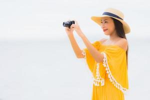 porträtt vacker asiatisk kvinna slitage hatt med leende glad fritid i ta ett foto på stranden och havet i semester semester