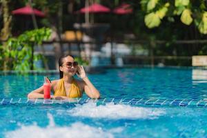 porträtt vacker ung asiatisk kvinna fritid koppla av leende med vattenmelon juice runt poolen i hotellort foto