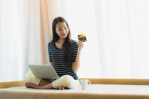 porträtt vacker ung asiatisk kvinna med dator anteckningsbok eller bärbar dator med kreditkort för shopping foto