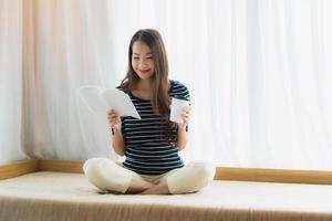 porträtt vacker ung asiatisk kvinna läsebok och hålla kaffekopp eller mugg i soffan i vardagsrummet foto