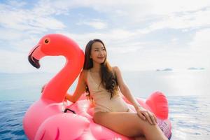 stående ung asiatisk kvinna på uppblåsbar flottörflamingo runt utomhuspool i hotellresort foto