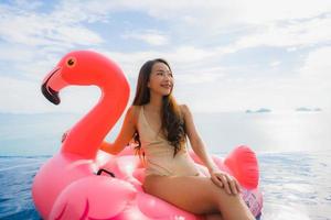 stående ung asiatisk kvinna på uppblåsbar flottörflamingo runt utomhuspool i hotellresort foto