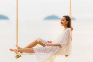 stående vacker ung asiatisk kvinna som sitter på gungan runt stranden havet för avkoppling foto