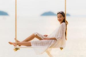 stående vacker ung asiatisk kvinna som sitter på gungan runt stranden havet för avkoppling foto