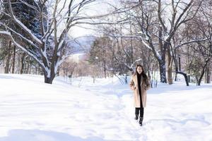 stående ung vacker asiatisk kvinna leende lycklig resa och njut av med snö vintersäsongen foto