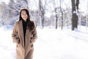 stående ung vacker asiatisk kvinna leende lycklig resa och njut av med snö vintersäsongen foto