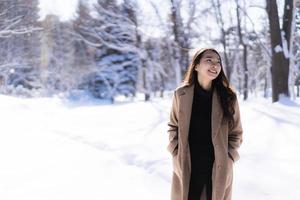 stående ung vacker asiatisk kvinna leende lycklig resa och njut av med snö vintersäsongen foto