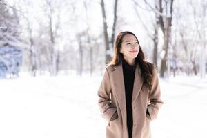 stående ung vacker asiatisk kvinna leende lycklig resa och njut av med snö vintersäsongen foto