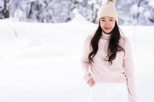 stående ung vacker asiatisk kvinna leende lycklig resa och njut av med snö vintersäsongen foto