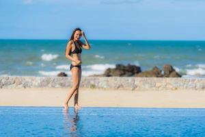 porträtt vacker ung asiatisk kvinna slitage bikini runt poolen i hotellort nästan havet ocean beach foto