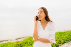 porträtt vacker asiatisk kvinna slitage hatt med leende glad för att prata mobiltelefon på stranden foto