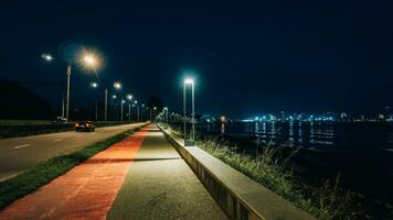 natt gata, brinnande lyktor. i de distans du kan ser de natt stad på de stranden. tömma atmosfärisk mystisk gående gata foto