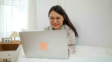 asiatisk frilans företag kvinna använder sig av bärbar dator uppkopplad företag i säng på Hem. foto