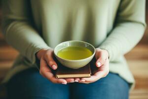 lugna scen av händer som vaggar en grön te kopp med en mindfulness bok närliggande ai generativ foto