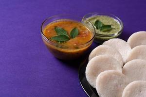 idli med sambar och kokosnötchutney på violett bakgrund, indisk maträtt sydindisk favoritmat rava idli eller semolina idly eller rava idly, serveras med sambar och grön chutney. foto