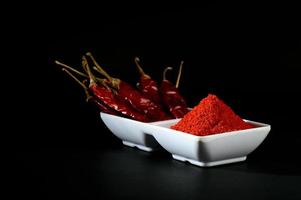 kyligt pulver med röd kylig i vit platta, torkade chili på svart bakgrund foto