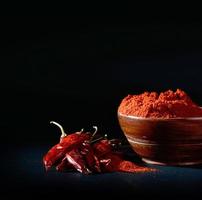kyligt pulver i träskål med röda kyliga, torkade chili på svart bakgrund