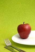 läckert äpple i tallrik med kniv och gaffel på grön bakgrund foto