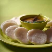 idli med sambar i skål på grön bakgrund, indisk maträtt sydindisk favoritmat rava idli eller semolina idly eller rava idly, serveras med sambar och grön kokosnötchutney. foto
