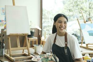 ung asiatisk kvinna konstnär i konst studio se på kamera och leende. foto