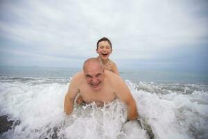 Lycklig pojke simmar och spelar med morfar på de strand. foto